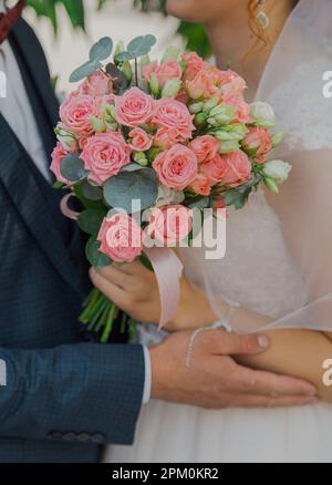 Heureux jeunes mariés tenant un bouquet dans leurs mains serrant leur jour de mariage Banque D'Images