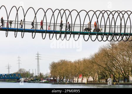 Oberhausen, NRW, le 10th avril 2023. Deux marcheurs traversent le pont avec leurs trois grands chiens de race Old English Sheepdog. Les randonneurs apprécient un lundi de Pâques plutôt ensoleillé et doux sur le célèbre pont 'linky Springs to Fame' d'Oberhausen. Le pont piétonnier, long de 406 mètres et traversant le canal Rhin-Herne, a été conçu par l'artiste Tobias Rehberger. Il est illuminé la nuit et aurait été inspiré par le jouet slinky. Credit: Imagetraceur/Alamy Live News Banque D'Images