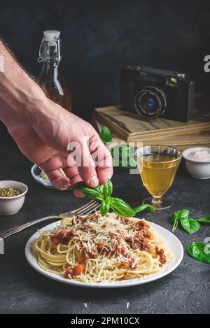 Spaghetti à la sauce bolognaise et parmesan râpé. Garnir à la main le repas préparé avec des feuilles de basilic Banque D'Images