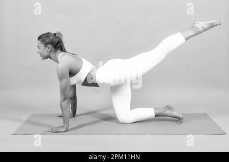 Femme de yoga prend des cours de yoga. Une jeune fille sportive paisible dans des vêtements de sport qui s'exercent sur un tapis. Arrière-plan gris isolé. Banque D'Images