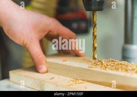 Gros plan de la perceuse et du foret doré à côté d'un morceau de planche en bois et de limaille de bois. Main de menuisier dans le plan. Photo de haute qualité Banque D'Images