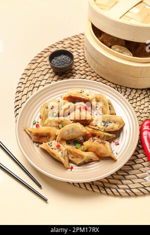 Assiette avec savoureuse jiaozi chinoise, piment rouge et cuiseur vapeur en bambou sur fond beige Banque D'Images