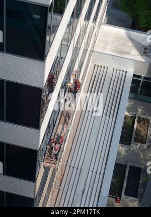 Vue en grand angle de deux lave-glaces qui nettoient les fenêtres d'un immeuble de bureaux dans les Woodlands, Texas, tout en étant debout sur un échafaudage suspendu. Banque D'Images