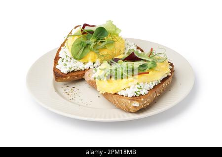 Assiette avec délicieux œufs brouillés sandwiches et verts sur fond blanc Banque D'Images