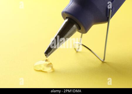 La colle fondue s'égoutte de la buse du pistolet sur fond jaune, gros plan Banque D'Images