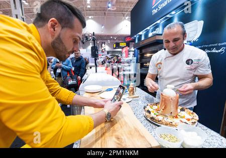 Toronto, Canada. 10th avril 2023. Un homme (L) prend des photos d'une pizza fraîchement cuite lors du salon des restaurants du Canada (RC Show) de 2023 à Toronto, au Canada, sur 10 avril 2023. Cet événement de trois jours, qui a débuté lundi, présente des produits de pointe et une large gamme de plats et de boissons. Credit: Zou Zheng/Xinhua/Alamy Live News Banque D'Images