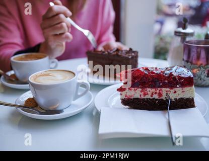 Berlin, Allemagne. 27th mars 2023. Une femme fait un morceau de gâteau avec une fourchette à gâteau tandis qu'un autre morceau de gâteau et deux cappuccini s'assoient sur la table dans un café de Prenzlauer Berg. Selon leurs propres déclarations, une proportion considérable d'adultes mangent moins de bonbons depuis la crise de Corona. (À l'enquête dpa: 'Un bon quartier mange moins de bonbons depuis Corona') Credit: Annette Riedl/dpa/Alay Live News Banque D'Images