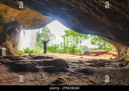 Vue arrière d'un homme à l'intérieur d'une grotte contre une chute d'eau à Sipi Falls, Kapchorwa, Ouganda Banque D'Images