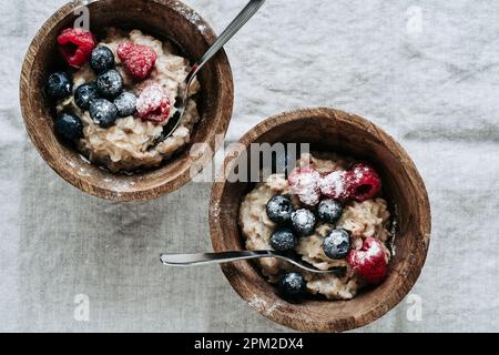 Porridge de flocons d'avoine avec myrtille fraîche, baies de framboises dans un bol en bois sur toile de lin, gros plan. Nourriture saine, petit déjeuner, vue du dessus Banque D'Images