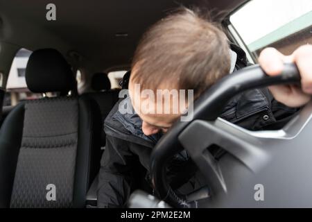 Jeune homme d'affaires barbu assis en voiture très contrarié et stressé après une défaillance difficile et se déplaçant dans l'embouteillage Banque D'Images