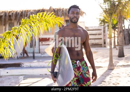 Portrait d'un homme afro-américain heureux tenant une planche de surf et souriant à la plage, avec un espace de copie Banque D'Images