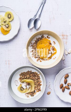 Bols de céréales au yaourt avec kiwi et fruits orange sur bois blanc, vue du dessus. Repas végétarien sain pour le petit déjeuner Banque D'Images