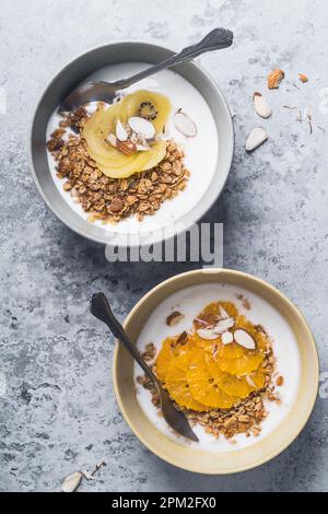 Bols de céréales au yaourt avec kiwi et fruits orange sur fond gris, vue du dessus. Repas végétarien sain pour le petit déjeuner Banque D'Images