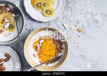 Bols de céréales au yaourt avec kiwi et fruits orange sur fond gris, vue du dessus. Repas végétarien sain pour le petit déjeuner Banque D'Images