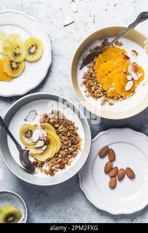 Bols de céréales au yaourt avec kiwi et fruits orange sur fond gris, vue du dessus. Repas végétarien sain pour le petit déjeuner Banque D'Images