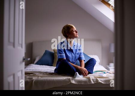 Femme réfléchie portant des infirmières ou des médecins uniforme assis sur le lit à la maison Banque D'Images
