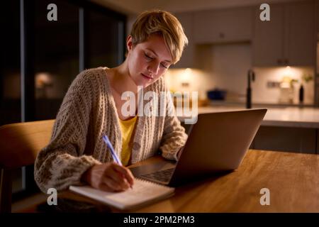 Jeune femme travaillant ou étudiant sur un ordinateur portable à la maison la nuit Banque D'Images
