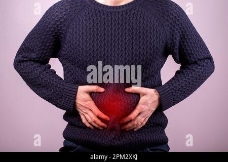 Homme souffrant de douleurs à l'estomac sévères assis à la maison. Main d'un homme mature tenant l'abdomen souffrant de douleur, de diarrhée ou de problème digestif. Peinture Banque D'Images