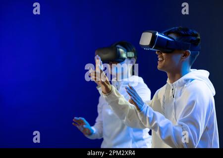 Homme et femme asiatiques heureux utilisant des micro-casques vr en studio avec lumière bleue et espace de copie Banque D'Images