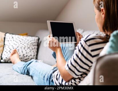 Femme tenant une tablette dans ses mains et regardant l'écran tout en étant allongé sur un canapé. Banque D'Images