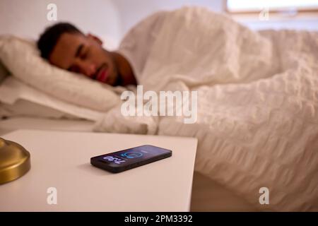 Homme à la maison endormi au lit avec alarme sur téléphone portable Banque D'Images