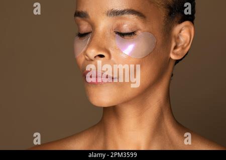 Soin du visage. Femme noire d'âge moyen avec des timbres cosmétiques appliqués sous les yeux prenant soin du visage, hydratant la peau Banque D'Images