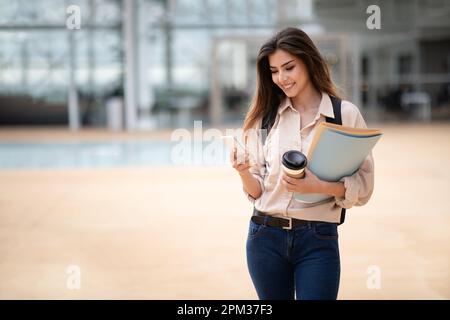 Bonne jeune femme caucasienne brunette étudiant dans une ambiance décontractée avec sac à dos, livres et smartphone Banque D'Images