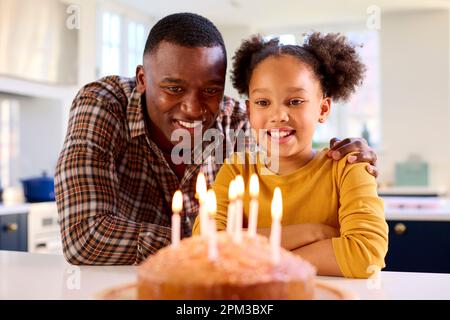 Père et fille à la maison dans la cuisine célébrant des bougies soufflantes sur le gâteau d'anniversaire fait maison Banque D'Images