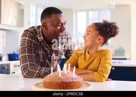 Père et fille à la maison dans la cuisine célébrant des bougies soufflantes sur le gâteau d'anniversaire fait maison Banque D'Images