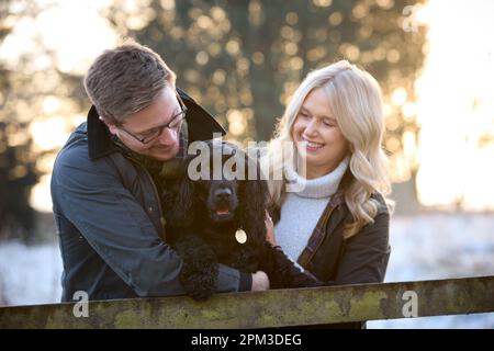 Couple aimant avec chien d'épagneul en canine penchée sur Fence lors d'une promenade en neige dans la campagne d'hiver Banque D'Images