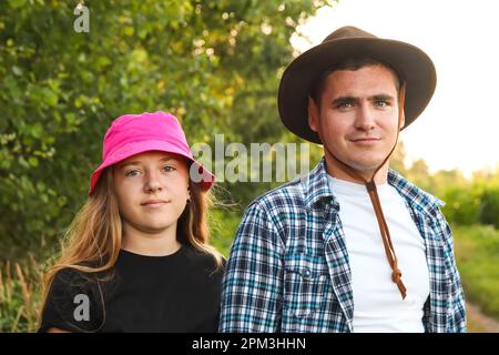 Sœur et frère enjoué avec cowboy et chapeau panama. Ils sont à la nature flou d'arrière-plan à l'extérieur, dans des tenues décontractées. Portraits Banque D'Images