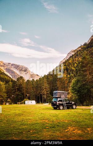 Une voiture tout-terrain en 4x4 campée dans une vallée avec une vue imprenable sur la forêt et les montagnes au coucher du soleil. Voyage en minibus et en plein air l'été Banque D'Images