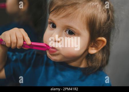 Portrait en gros plan d'une petite fille adorable portant un t-shirt bleu tenant une brosse à dents et apprenez à se brosser les dents le matin à la maison. Entretien des dents Banque D'Images