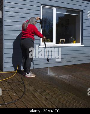 Femme nettoyant le pont en bois avec un nettoyeur haute pression Banque D'Images