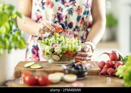 Une femme prépare une salade saine et met une tomate en tranches dans un bol. Banque D'Images