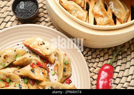 Assiette avec savoureuse jiaozi chinoise, piment rouge et cuiseur vapeur en bambou sur table Banque D'Images