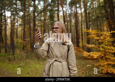 Femme à la recherche de la couverture mobile sur le téléphone mobile se trouve dans une forêt d'automne, pas d'écran de service Banque D'Images