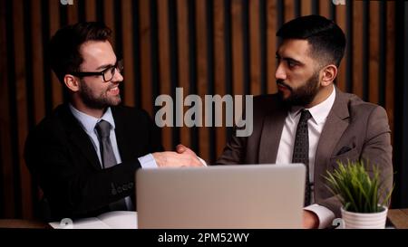 Deux jeunes hommes sourient et se secouent la main lorsqu'ils se rencontrent à la table du bureau de l'entreprise Banque D'Images