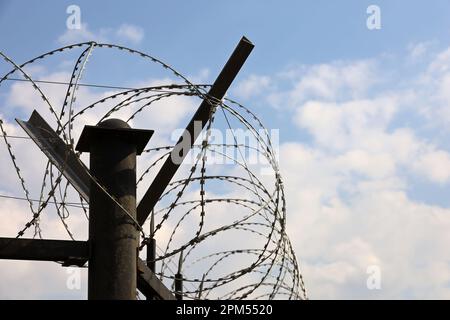 Fil barbelé sur fond de ciel bleu avec nuages. Concept de frontière, de prison, de guerre ou d'immigration Banque D'Images