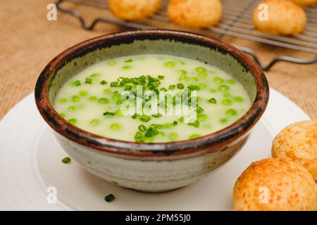 Soupe à la crème de céleri avec un pois vert dans un bol garni d'oignon vert haché et servi avec du pain au fromage fraîchement cuit en gros plan sur l'onglet de la cuisine Banque D'Images