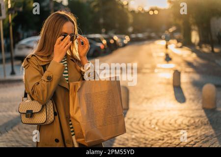 Une femme se promène dans la ville après avoir fait du shopping au coucher du soleil avec un sac en papier Banque D'Images