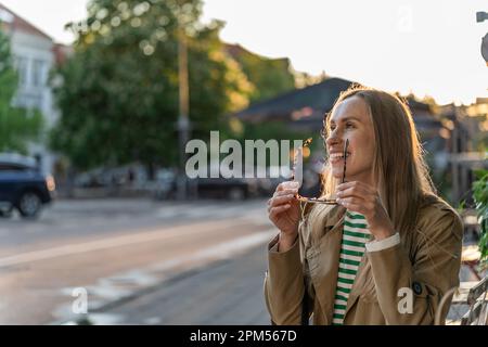 Une femme est assise dehors, souriant et mettant des lunettes de soleil Banque D'Images