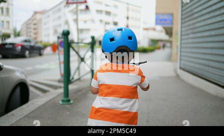 Arrière de l'enfant à cheval jouet dans la rue portant un casque. Sportive, garçon de 2 ans, utilise des équipements de transport à l'extérieur Banque D'Images