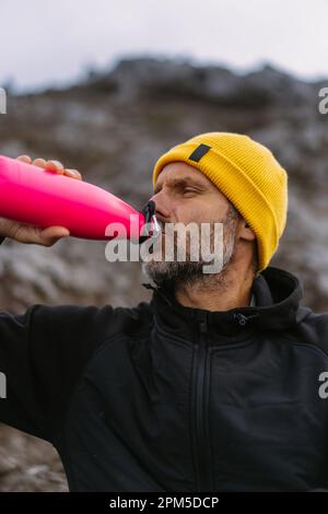 L'homme se repose dans les montagnes, boit de l'eau et récupère Banque D'Images