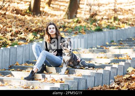 une jeune femme marche son chien dans un parc d'automne plein de feuilles Banque D'Images