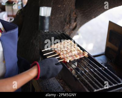 Main tenant des bâtonnets de porc grillés sur feu flamboyant dans poêle en acier Banque D'Images