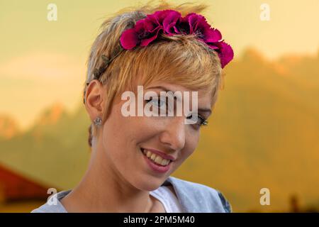 Gros plan portrait d'une femme aux cheveux blonds courts, ordonné et fait, portant un bandeau fait de fleurs fuchsia, sur un fond extérieur qui Banque D'Images