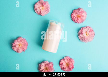 Distributeur blanc cosmétique et fleur de sakura sur fond bleu. Concept de cosmétiques naturels. Vue de dessus, plan d'agencement, maquette. Banque D'Images