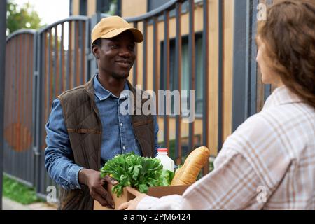 Portrait à la taille de jeune homme noir en train de remettre une boîte à provisions fraîches à une jeune femme en ville Banque D'Images
