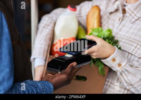 Gros plan de la jeune femme qui paie pour la livraison d'épicerie par téléphone intelligent, espace de copie Banque D'Images